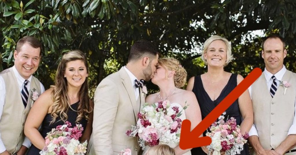 Les jeunes mariés échangent un baiser pour la photo. Mais regardez la petite fille aux fleurs, elle vole la vedette !