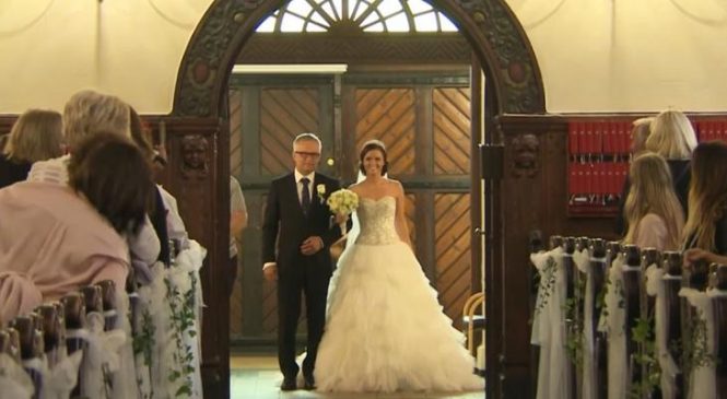 La mariée descend l’allée avec son père, mais regardez bien ce qu’elle tient dans la main gauche!